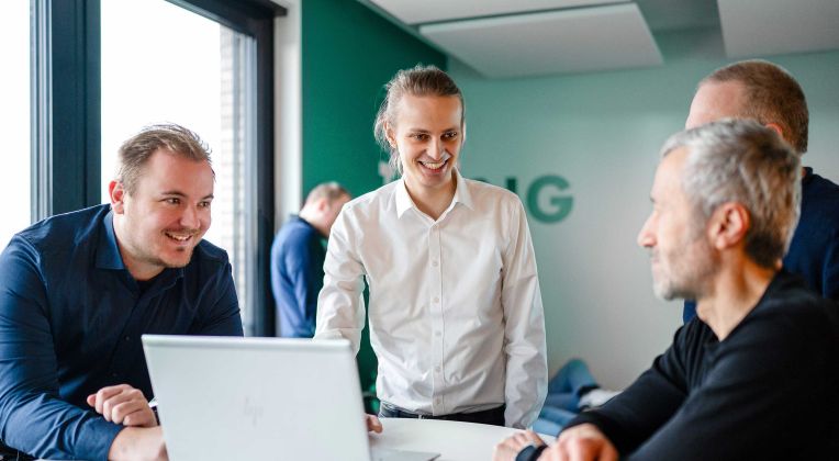 Mitarbeiter stehen und sitzen an einem Tisch mit Laptop