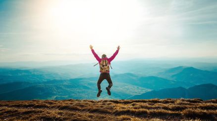 Ein dynamisches Bild mit einem Mann, der vor einer Berglandschaft mit Weitblick hochspringt.