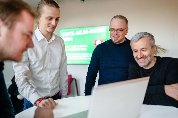 Eine Gruppe von Personen stehen um einen aufgeklappten Laptap herum.