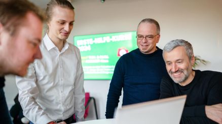 Eine Gruppe von Personen stehen um einen aufgeklappten Laptap herum.