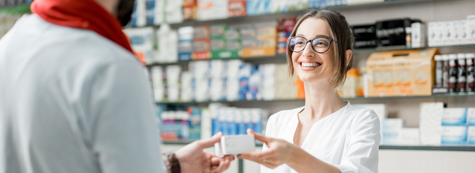 Eine junge Apothekerin reicht einem Kunden eine Packung