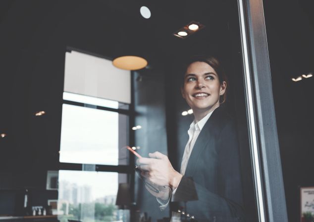 Eine Frau lehnt an einem Fenster und hält ein Tablet in der Hand.