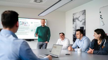 Mitarbeiter stehen und sitzen an einem Konferenztisch