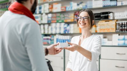 Eine junge Apothekerin reicht einem Kunden eine Packung