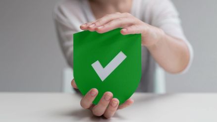 Zwei Hände halten ein Schild mit einem Häkchen darauf, symbolisierend Datenschutz und Sicherheit bei Künstlicher Intelligenz.