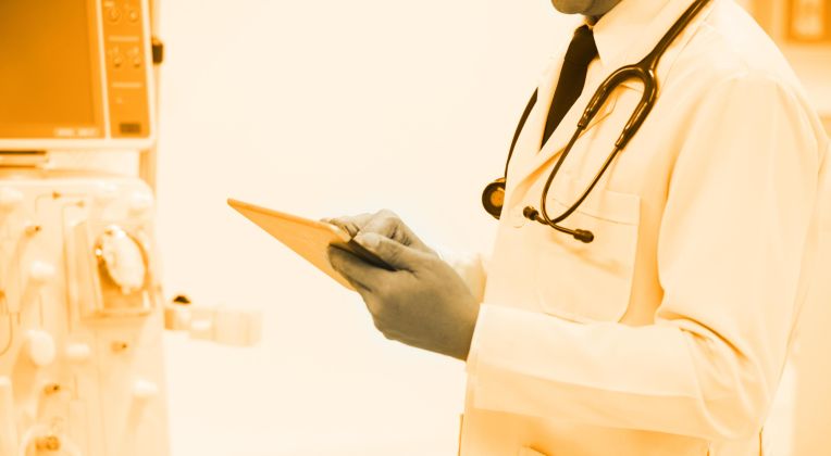 Arzt mit weißem Kittel und Stethoskop steht mit einem Tablet in der Hand vor einer Maschine zur Blutwäsche