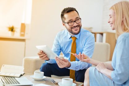 Ein Mann in Business Kleidung berät eine Frau, während er ein Tablet in der Hand hält.