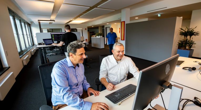 AKQUINET employees exchange ideas while sitting in front of a computer.