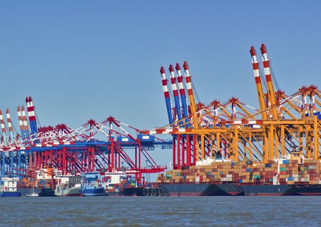 Terminal with many cranes and ships loaded with containers.