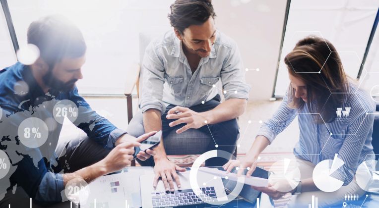 Zwei Männer und eine Frau schauen sich Informationen auf einem Notebook und Handy an.