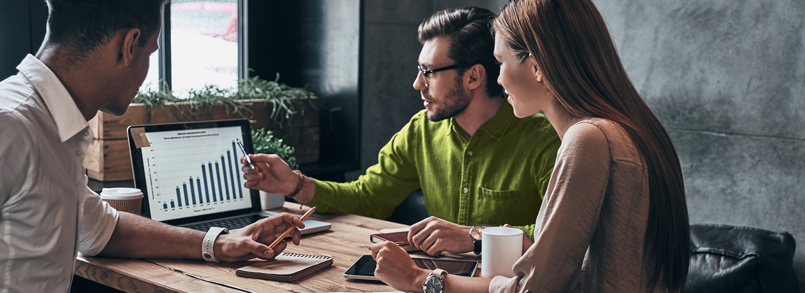 Drei BI Mitarbeitende sitzen zusammen an einem Tisch und beraten sich über die Datenanalyse an einem Labtop.