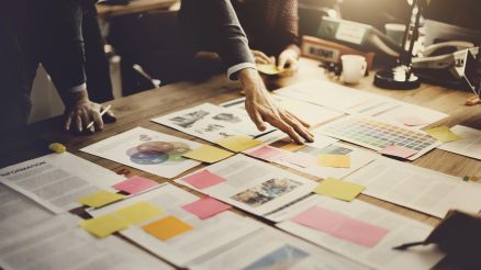 There are pieces of paper and information on a table, which two people are sorting through.