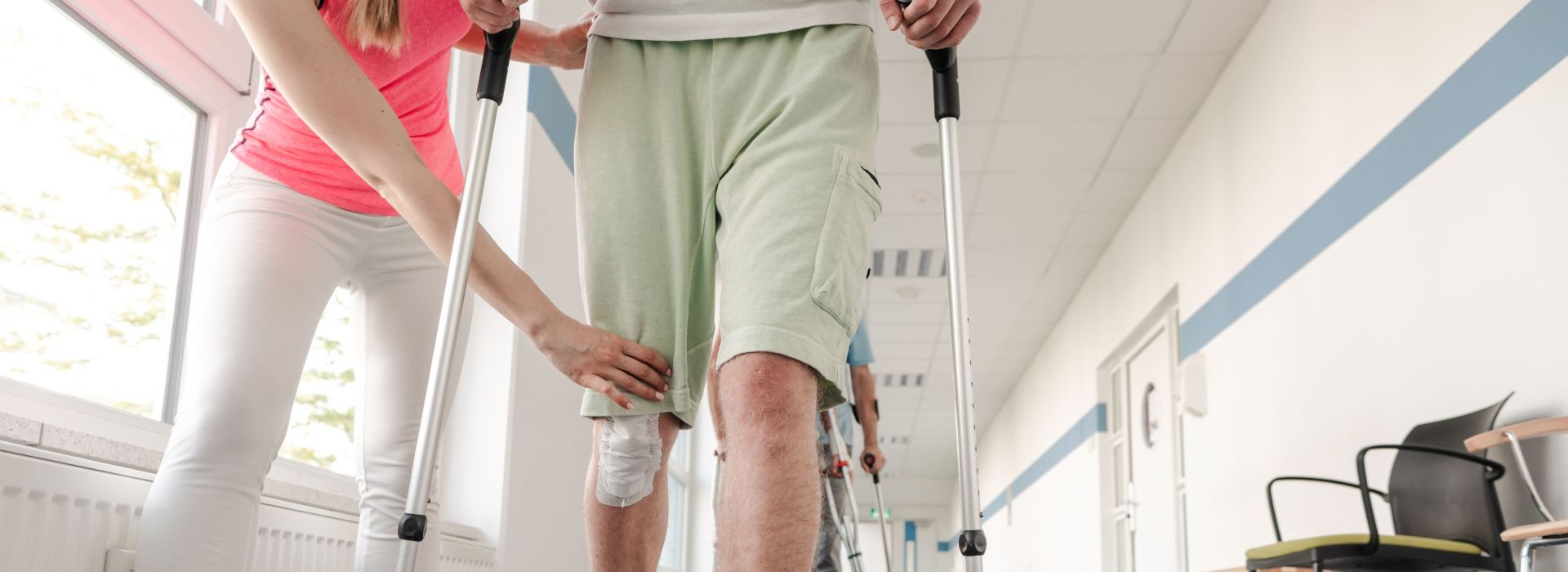 Ein junger Mann mit einer Knieverletzung geht an Krücken und wird von einer Frau unterstützt