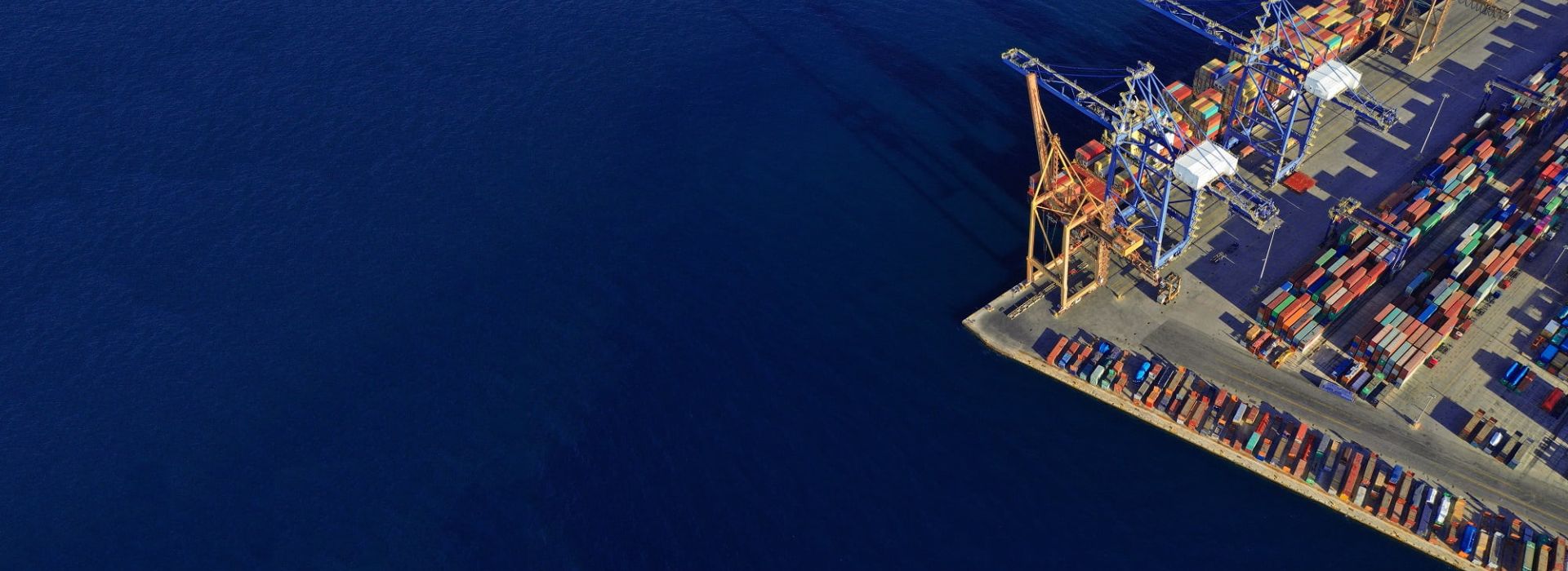 Dunkelblaues Wasser. Am rechten Rand die Ecke eines Terminals mit Containern und Kränen.