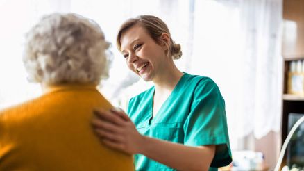 Pflegerin besucht alte Patientin zu Hause und legt ihre Hand auf den Rücken