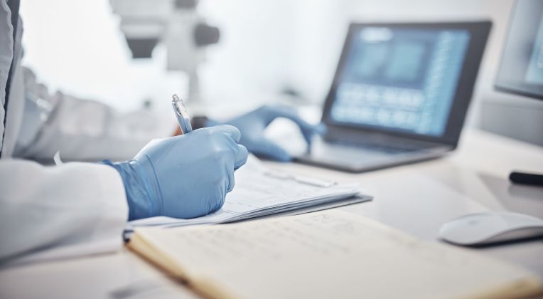 Eine Person mit medizinischen Handschuhen arbeitet an einem Laptop