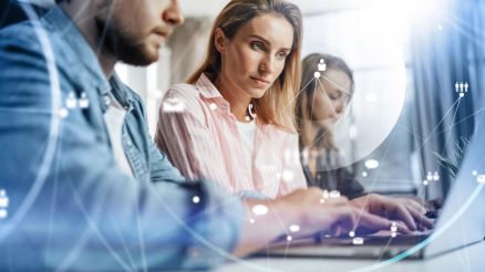 Zwei Frauen und ein Mann arbeiten an einem Notebook.