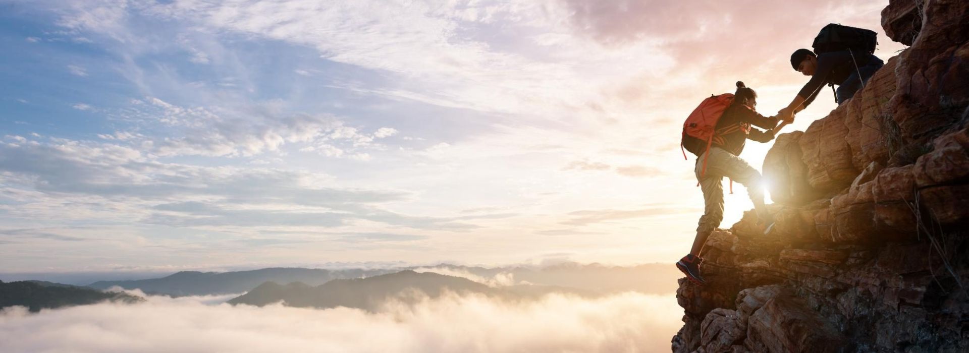 Personen helfen sich gemeinsam auf einen Berg zu steigen, stimmungsvoll mit Sonnenuntergang.