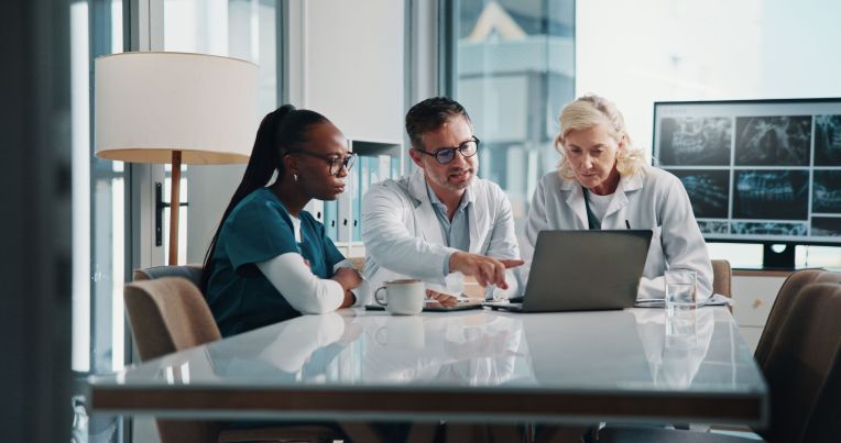 Zwei weibliche und ein Männlicher Arzt sitzen zusammen an einem Tisch und Nutzen das PVS LifeTime Cloud