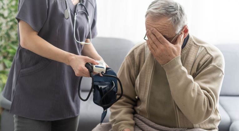 Ein älterer Mann bekommt von einer Pflegerin ein Blutdruckmessgerät gereicht.