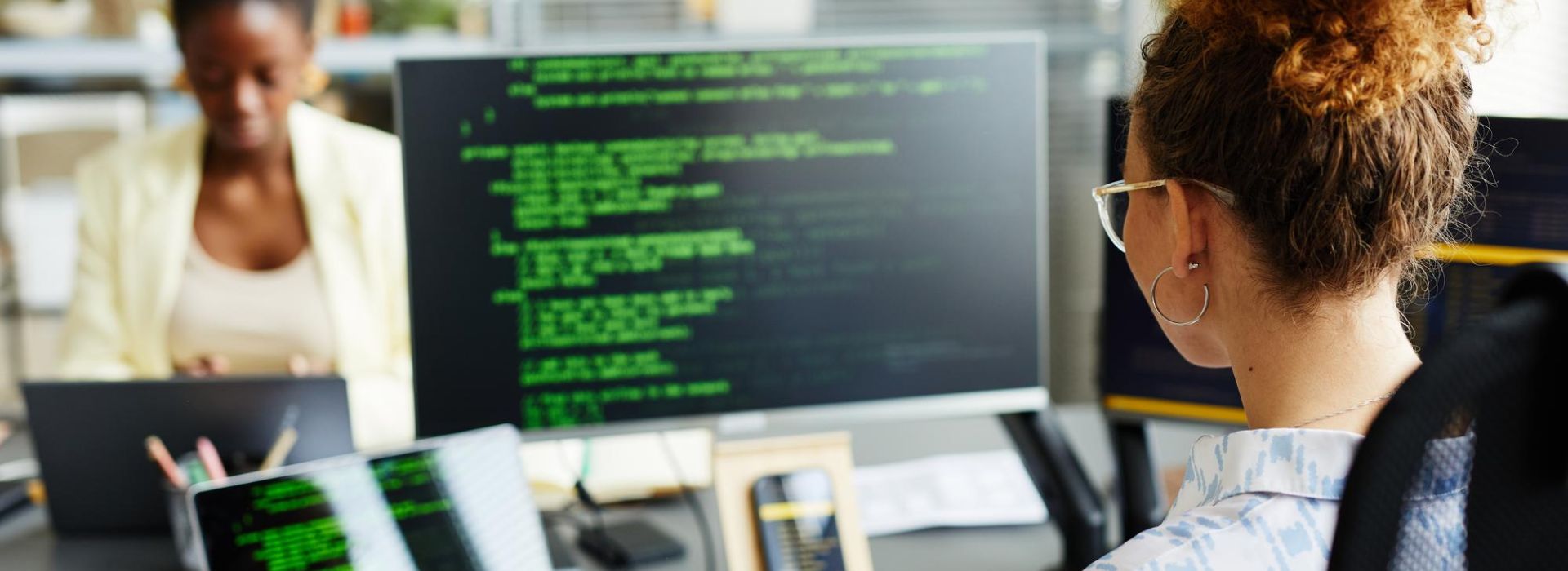 Eine Mitarbeiterin sitzt am Schreibtisch und schaut sich einen Code einer Automatisierungslösung auf zwei Bildschirmen an.