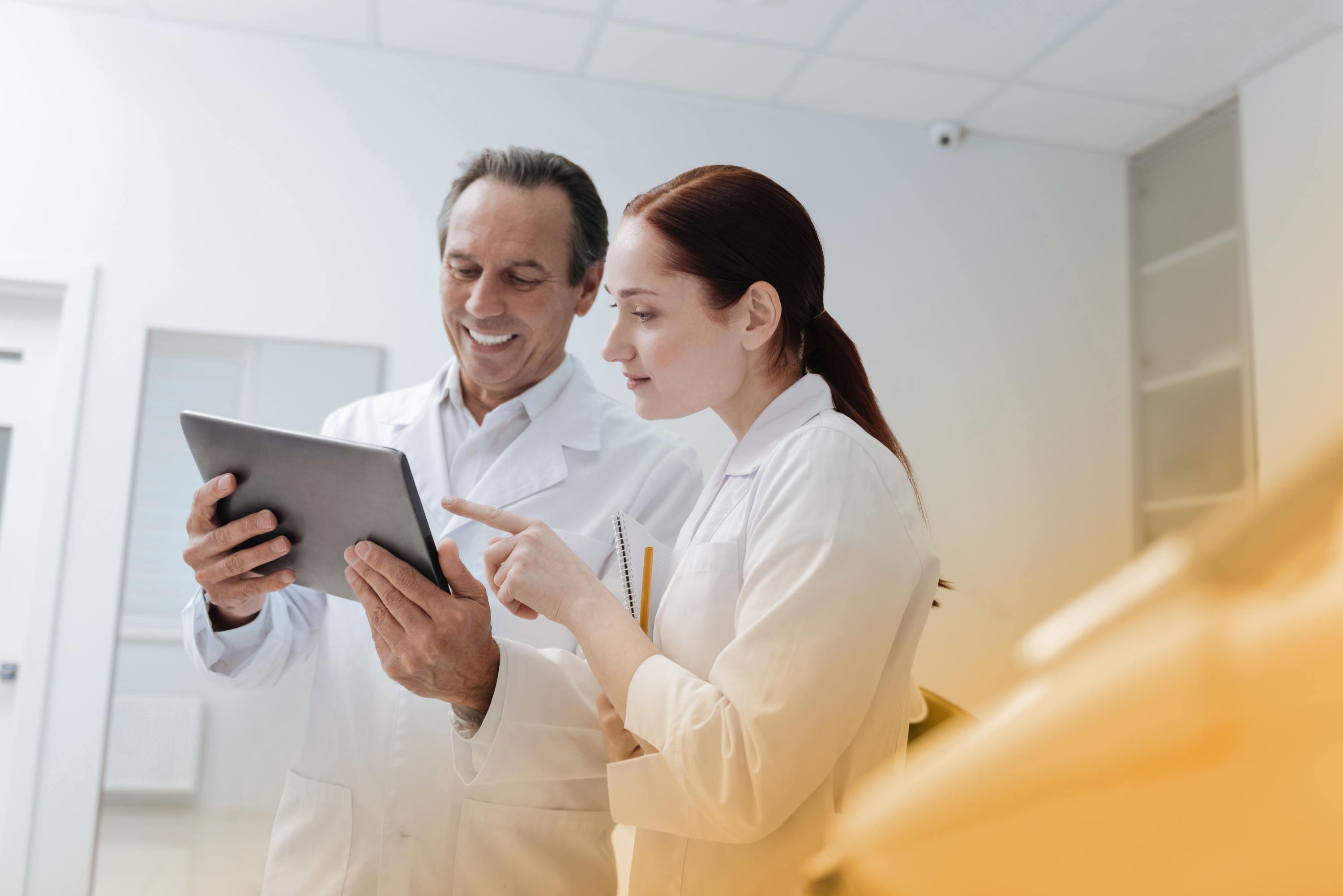 Eine Ärztin und ein Arzt schauen sich gut gelaunt medizinische Daten auf einem Tablet an