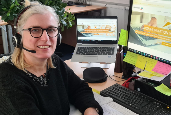 Mitarbeiterin sitzt am Schreibtisch vor ihrem Laptop und hat ein Headset auf dem Kopf