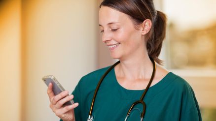 Doctor with stethoscope around her neck smilingly reads a short message on her smartphone