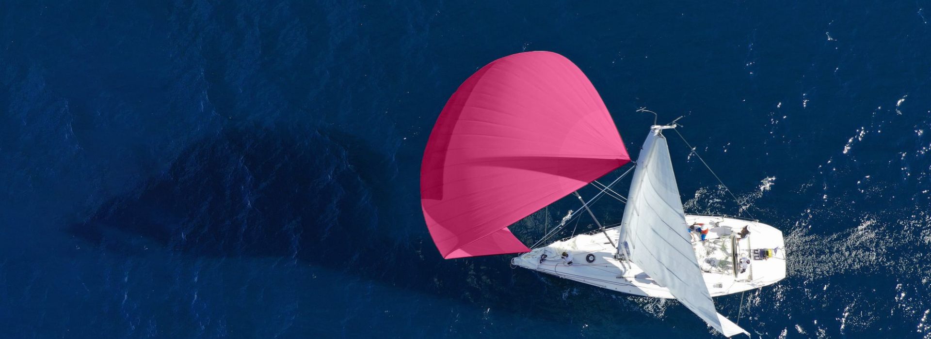 A white sailing ship with a big pink spinnaker on blue sea.