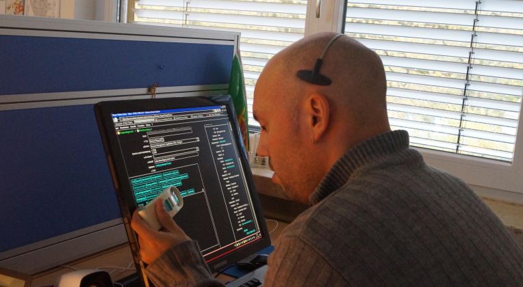 Inklusion und AKQUINET - ein Selbstverständnis. Ein Mitarbeiter der AKQUINET arbeitet aufgrund seiner Sehbehinderung mit Hilfe einer Bildschirmlupe an einem digitalen Arbeitsplatz.